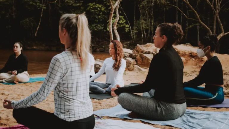 Grupo meditando sentado na areia à beira do rio