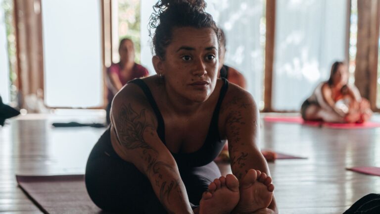 Mulher em alongamento sentada durante aula de yoga em sala de madeira