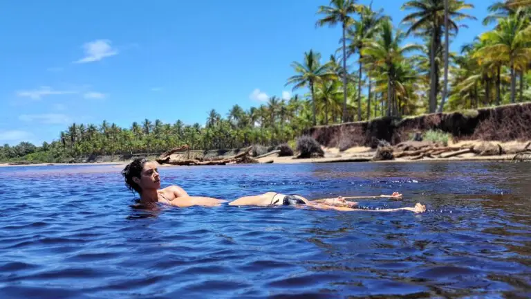 Mulher boiando em rio de águas escuras cercado de coqueiros