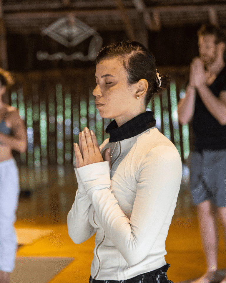 Mulher de olhos fechados com as mãos unidas em meditação dentro de uma oca