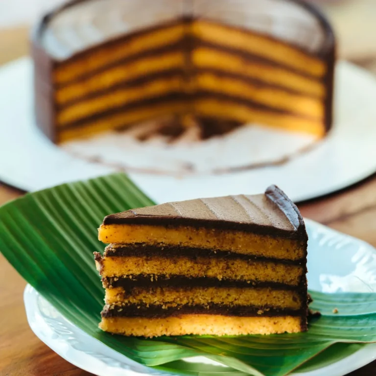 Fatia de bolo vegano em camadas com recheio de chocolate, servida sobre folha de bananeira no Karuh
