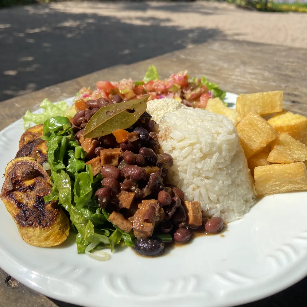 Prato vegano do almoço do Karuh ao ar livre, com feijão, arroz, mandioca, banana-da-terra e salada